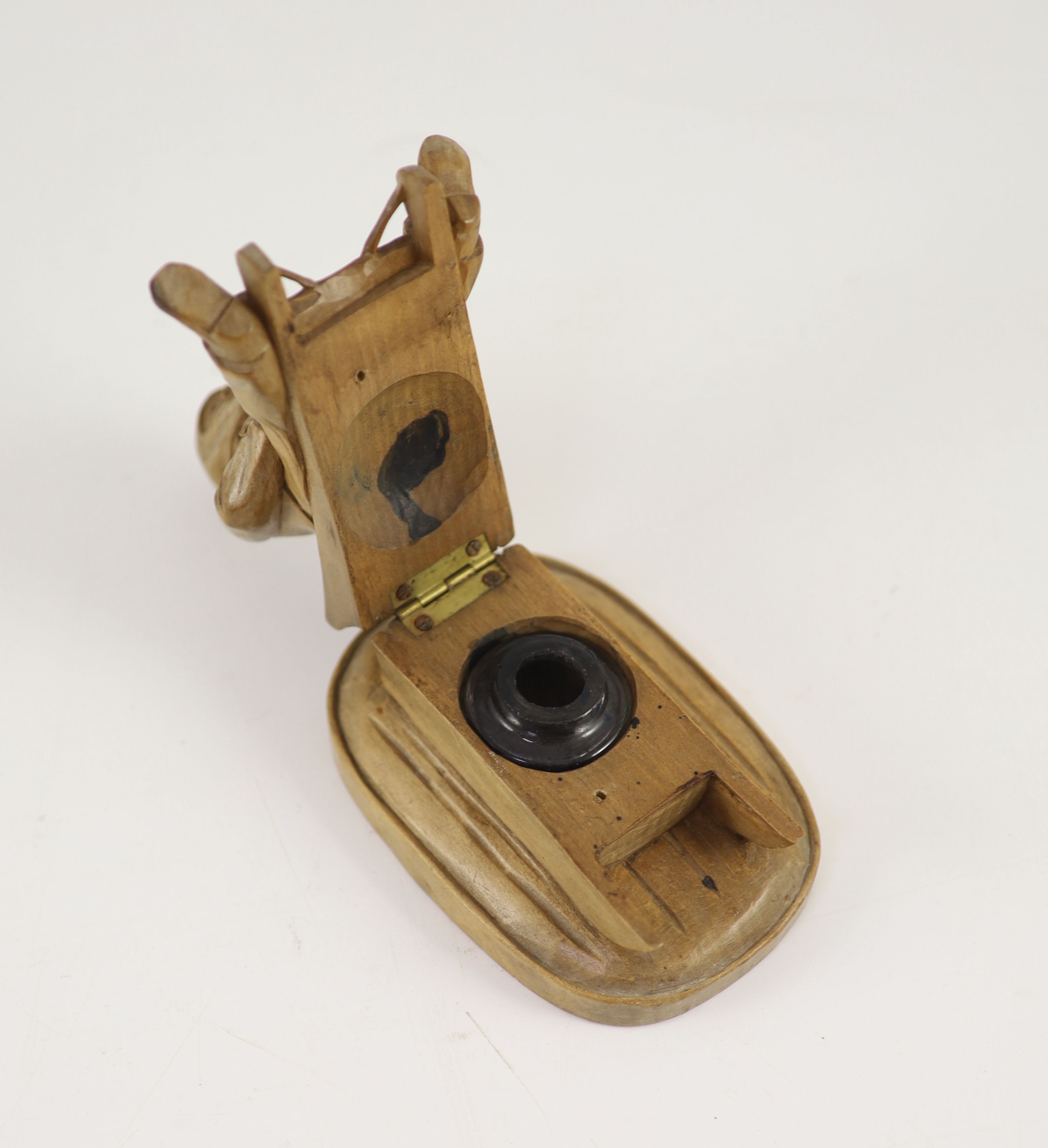 A North European novelty carved beech inkwell in the form of a seated figure sledging, c.1900, 11cm high, 11cm long.